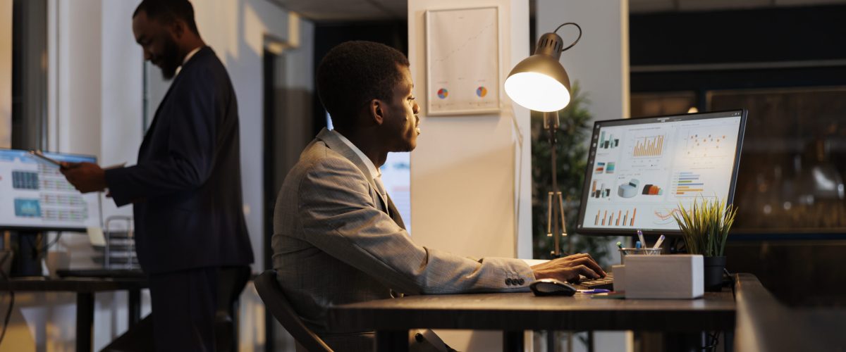 African american businessman looking at financial graphs report on computer, planning company investment typing business strategy. Executive manager working late at night in startup office