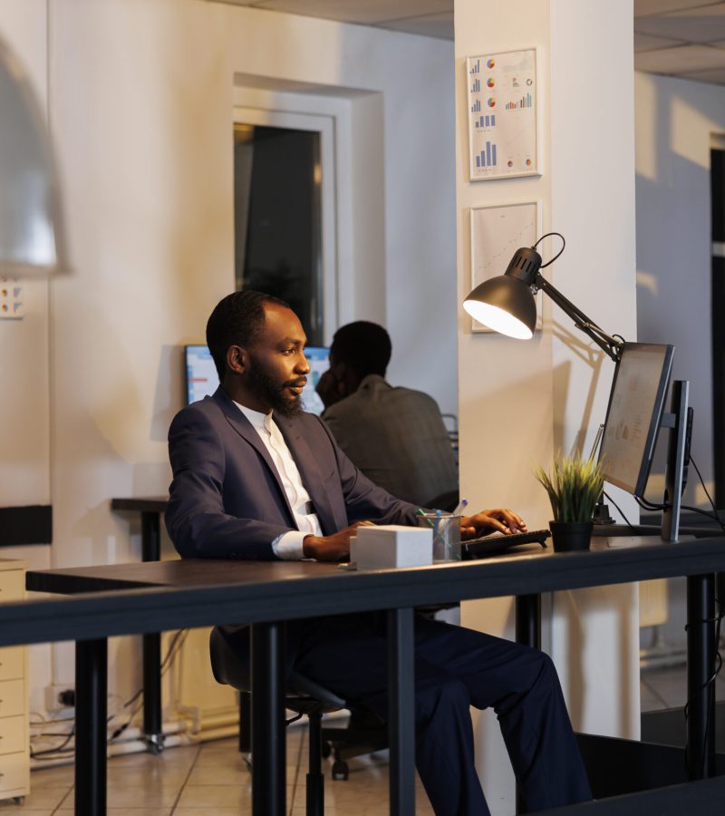 Entrepreneur analyzing marketing statistics working at financial growth report over hours in startup office. African american workers planning company strategy to increase business profit